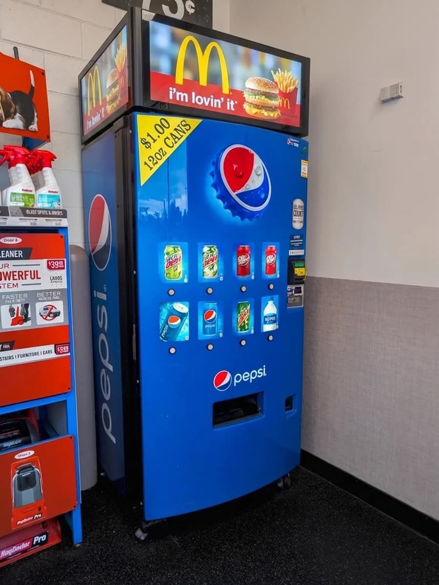 The same drinks machine with a lit advertising screen mounted above it.