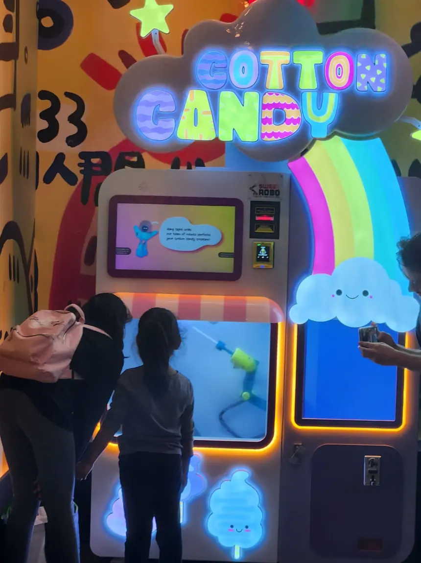 Two children working the controls of a cotton candy machine against a painted wall.