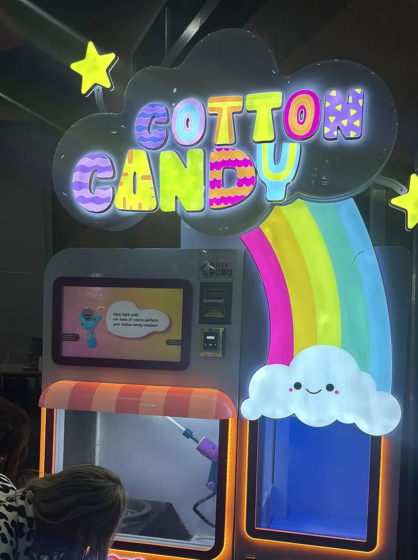 The lit sign and spinning head of a cotton candy machine on a venue floor.