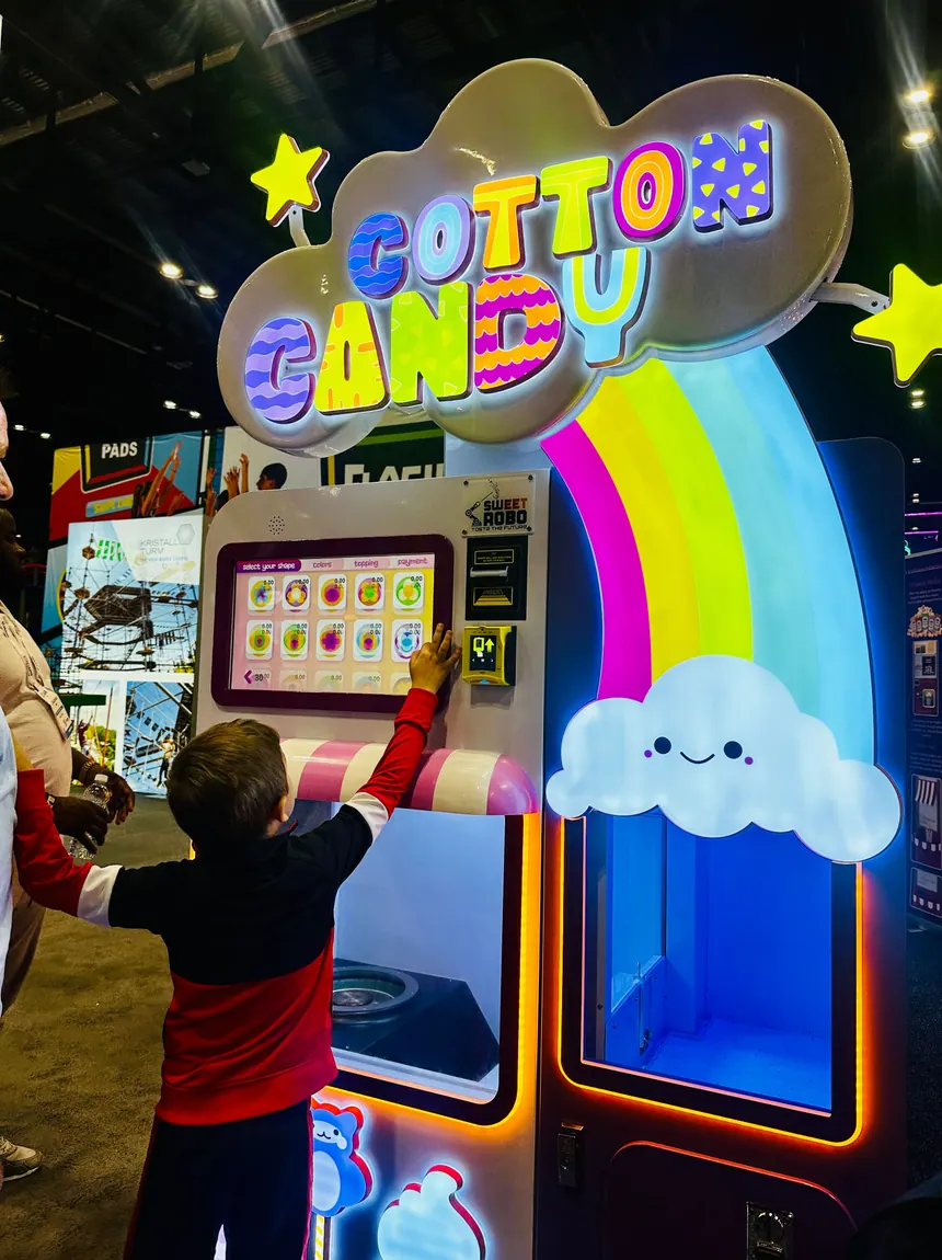 A small child reaching up to the touchscreen of a cotton candy machine.