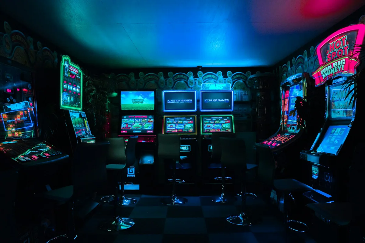 A row of arcade cabinets lit in blue and purple with a snack machine at the end of the aisle.