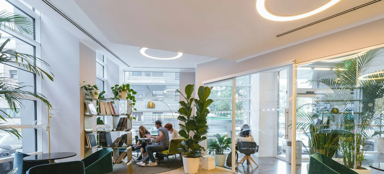 An open-plan office break area with tables, chairs and a kitchen counter along the back wall.